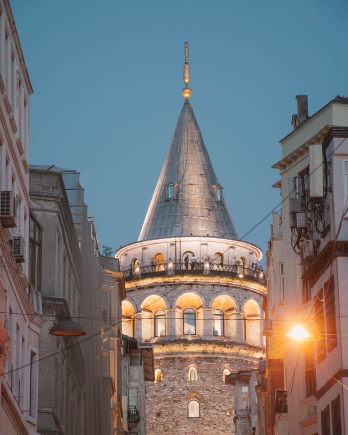 The iconic Galata Tower in Istanbul, beautifully illuminated at twilight with vibrant streetlight glow.